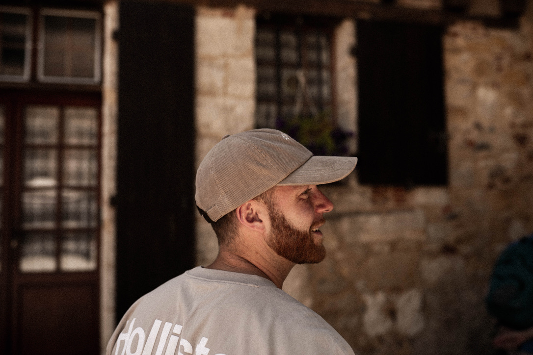 Alex de profil, casquette, devant une façade de pierre